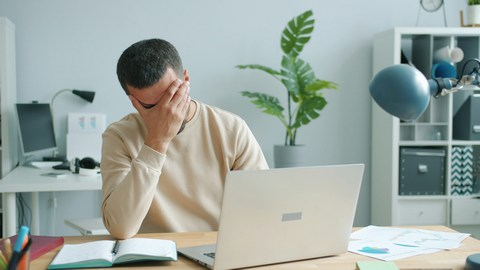 Frustrated man at desk with hand over face in despair